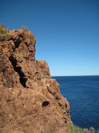Rock formation by sea against clear blue sky