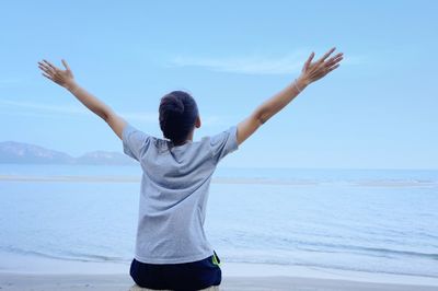 Rear view of woman sitting on shore at beach against sky