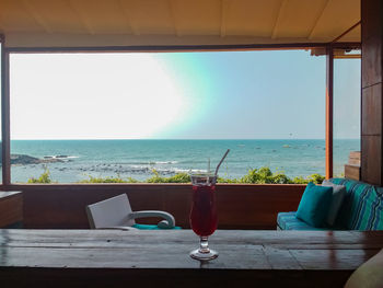 Table by sea against sky seen through glass window