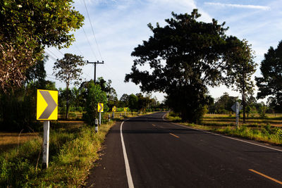 Road sign by trees against sky