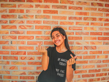 Portrait of a smiling young woman against brick wall