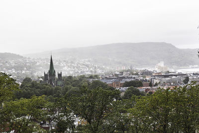 Trees and buildings in city against sky