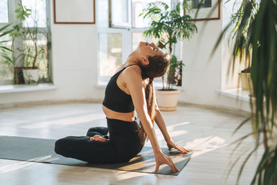 Young fit woman practice yoga doing asana in light yoga studio with green house plant