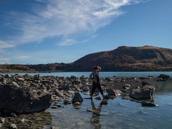 Woman shielding eyes while standing on rocks by lake