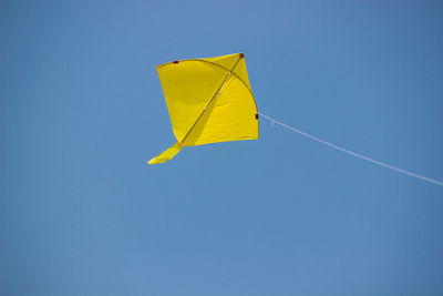 Low angle view of yellow kite flying against clear blue sky