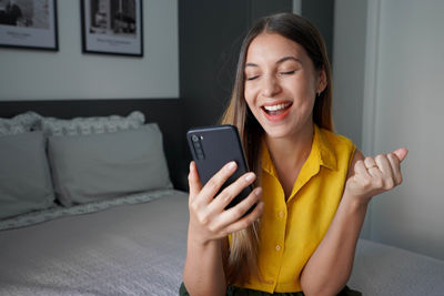 Woman excited for success holding smartphone with fist up and eyes closed celebrating victory 