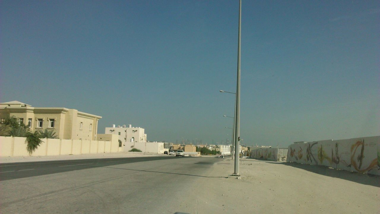 architecture, building exterior, built structure, clear sky, copy space, road, the way forward, street, blue, transportation, road marking, empty, street light, sunlight, day, outdoors, diminishing perspective, building, house, sky