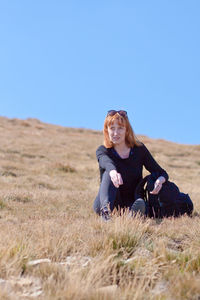 Woman looking away while sitting on field against clear sky during sunny day