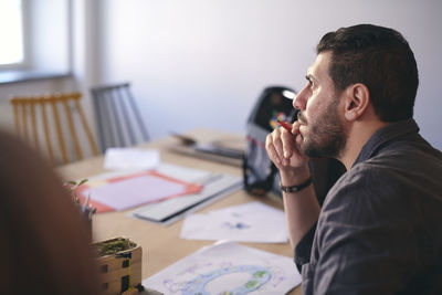 Side view of male engineer thinking while sitting with diagram at table in office