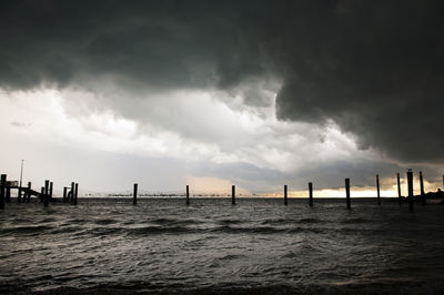 Wooden posts in sea against sky