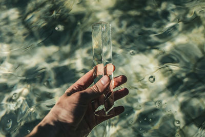 Cropped image of hand holding glass against water