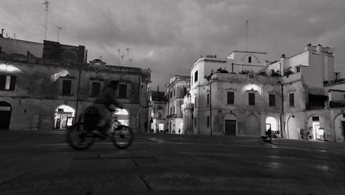 Man cycling on road against sky in city