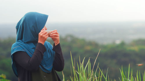 Woman holding umbrella on field against sky