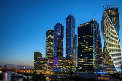 Low angle view of illuminated buildings against clear blue sky. moskva-city