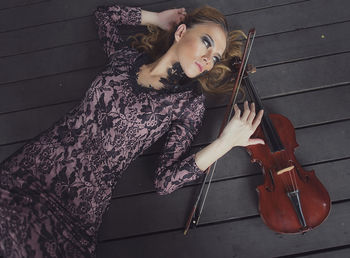 High angle view of young woman lying with violin on hardwood floor