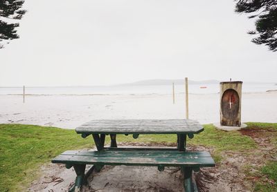 Chairs and table on beach against clear sky