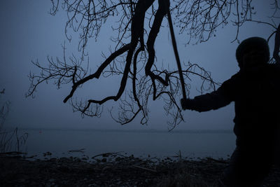 Silhouette man standing by bare tree against clear sky during sunset