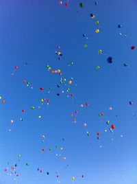 Low angle view of helium balloons flying against clear blue sky