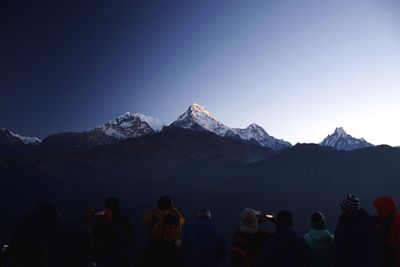 Group of people on snowcapped mountains against clear blue sky