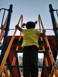 Rear view of girl climbing slide steps in playground against sky