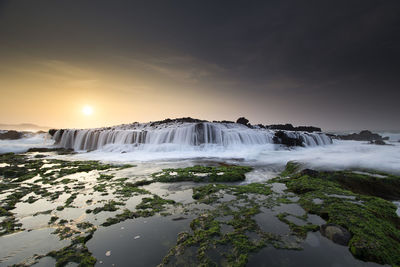 Scenic view of waterfall against sky during sunset