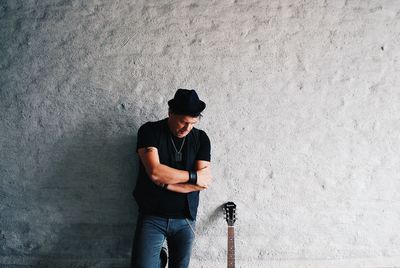 Young man looking away while standing against wall