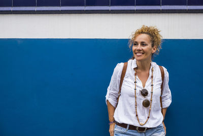 Smiling woman standing against blue wall outdoors