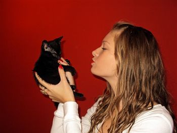 Close-up of woman holding black kitten against red wall