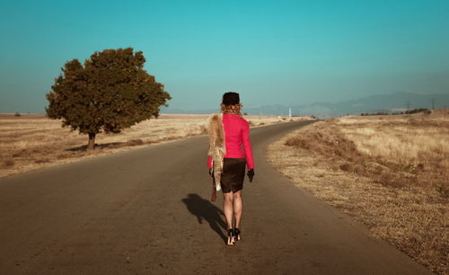 Rear view full length of woman walking amidst field on road