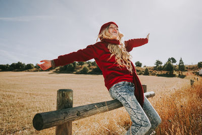 Woman with arms raised on field against sky