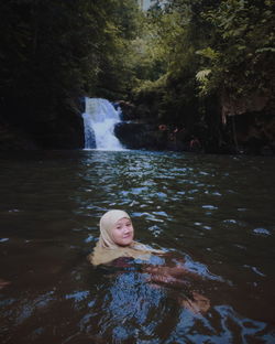 Portrait o woman sitting at pond against waterfall in forest