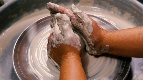 Soiled hands of a female potter working with a piece of white clay on a potter's wheel