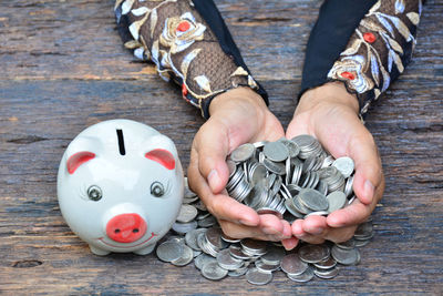 Cropped hands of woman holding money by piggy bank on wooden table