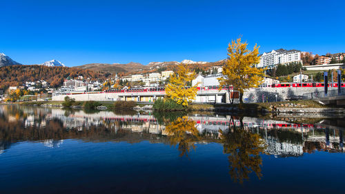 Scenic view of lake by buildings against clear blue sky