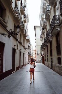 Rear view of young woman walking on street amidst buildings in city