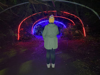 Rear view of woman standing against illuminated tunnel
