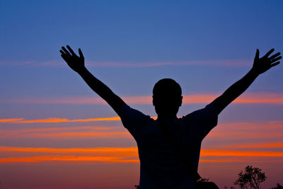 Silhouette man with arms outstretched standing against sky during sunset