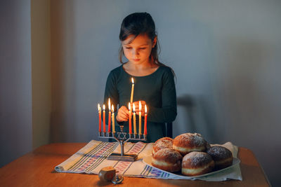 Girl lighting candles on menorah for traditional winter jewish hanukkah holiday at home. 