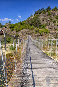 Footbridge leading towards mountains against sky