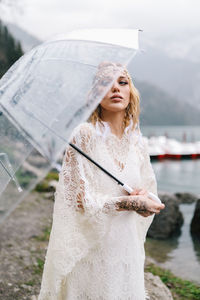 Beautiful young woman bride in a boho dress and with an umbrella stands in the rain in nature