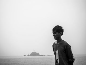 Young man standing on shore against clear sky