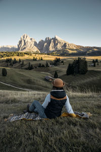 Rear view of man sitting on field against sky