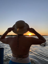 Rear view of woman standing at beach against sky during sunset