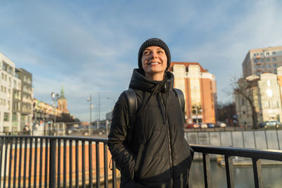 Smiling young woman in casual black jacket travelling with backpack. female walking on city street.