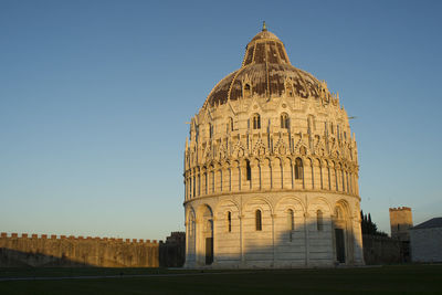 Pisa baptistery on field against clear blue sky in city