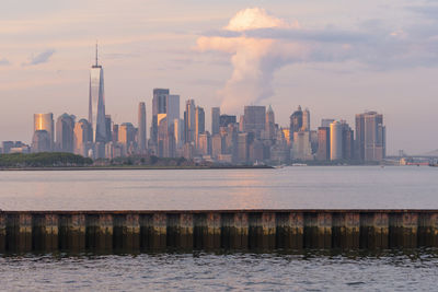 Sea by modern buildings against sky during sunset