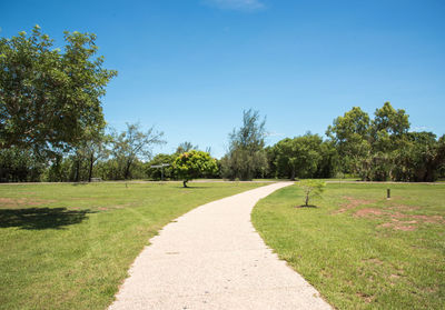 Footpath amidst trees on field against clear sky