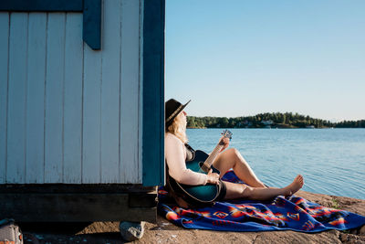 Woman sat in the sun on a rock playing the guitar