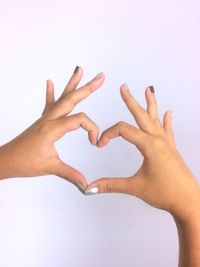 Cropped hands of woman forming heart shape over white background