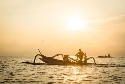 Silhouette people in sea against sky during sunset